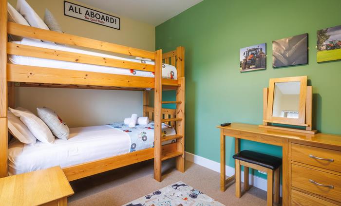 Full size single bunk bed with side table, dressing table and tractor-themed soft furnishings and tractor canvasses on wall.